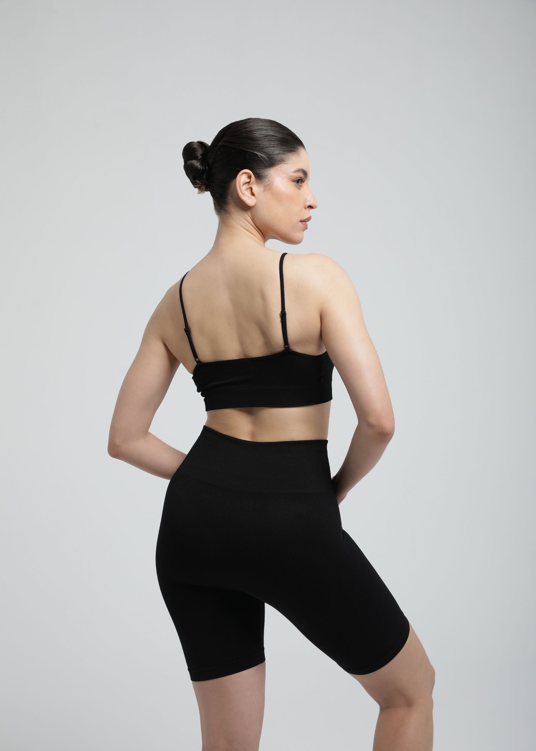 Second Skin high-waist sculpting biker short in graphite black, back view showing seamless fit.

Model wearing Second Skin Essential Sculpting Bralette in black, angled back studio pose